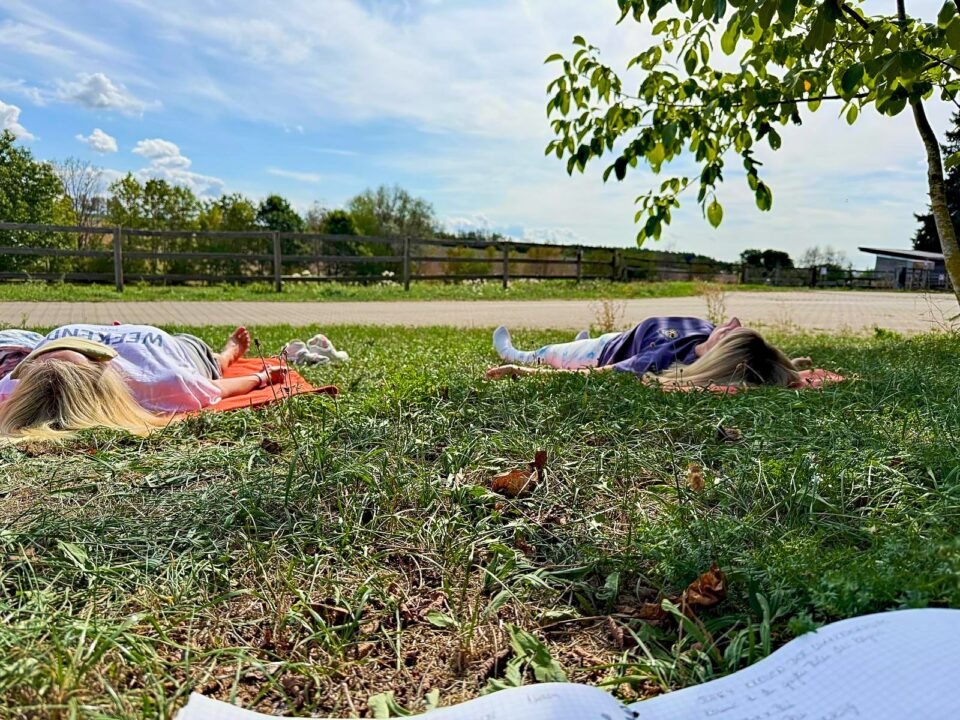 Zwei Teilnehmerinnen liegen bei der Yoga Nidra Praxis auf Yogamatten auf einer Wiese.